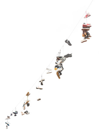 Many old worn boots or shoes hang on an electric cableの写真素材