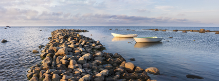 Two white oaring boats behind cobble stone pier in sea at sunsetの写真素材
