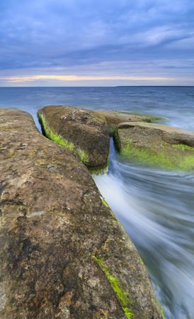 Large rocks covered with algae in sea at cloudy eveningの写真素材