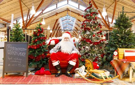 TALLINN, ESTONIA - DECEMBER 22, 2019: Santa claus sits between decorated fir trees in Balti Jaam market bulding in Tallinn Estonia in December 2019のeditorial素材