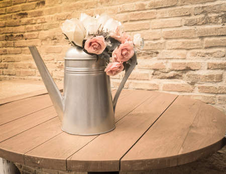 Bouquet of roses in watering can vase on wooden table, vintage style lightの写真素材