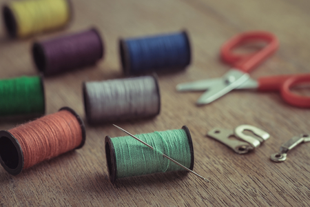 Thread with needle and scissors on wooden table, Vintage tone