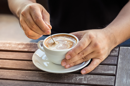 Man hand holding cup of coffee on old wooden tableの写真素材