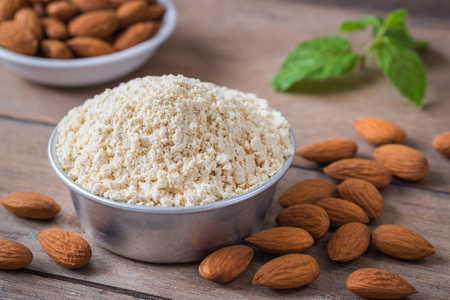 Almond flour in bowl and almonds on wooden tableの写真素材