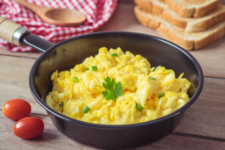 Scrambled egg in frying pan and toast on wooden tableの写真素材