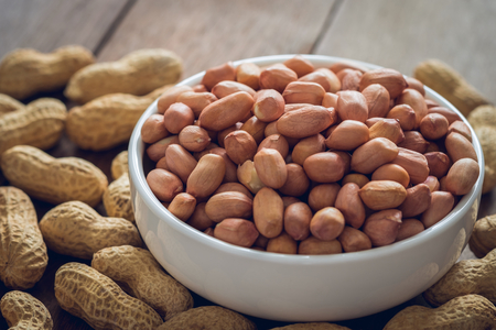 Raw peanuts in white bowl and peanut shell on wooden tableの写真素材