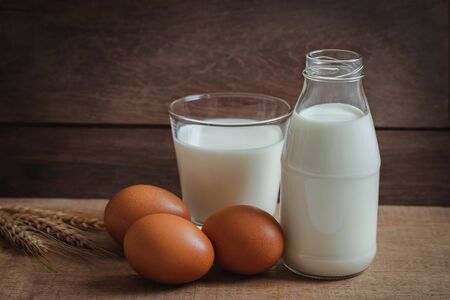 Milk bottle, glass of milk and egg on wooden tableの写真素材
