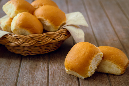 Soft bread rolls on wooden table and wicker basketの写真素材