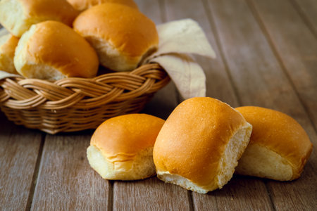 Soft bread rolls on wooden table and wicker basketの写真素材
