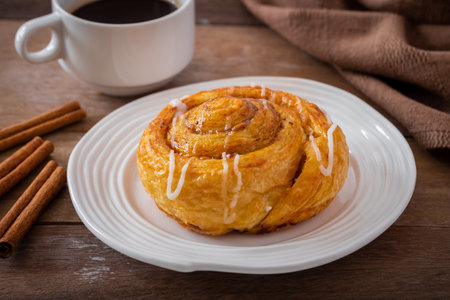 Cinnamon roll bun on white plate and cup of coffeeの写真素材