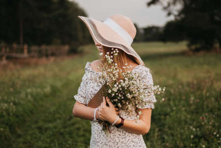 Beautiful girl in hat with bouquet of wildflowers in handの写真素材