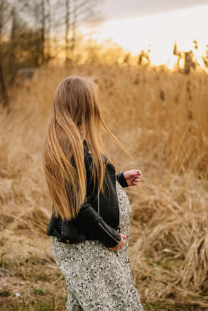 A young girl with long hair in a black leather jacket walks through the field.の写真素材