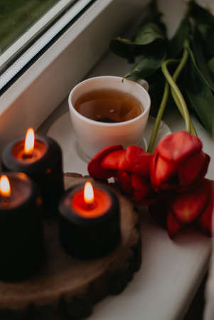 Cup of tea, red tulips and candles on the windowsillの写真素材