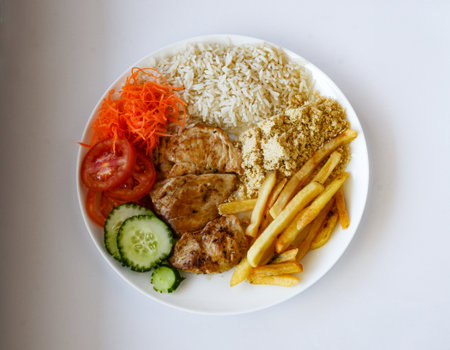 A white plate with tomato salad, cucumber, red carrots, french fries, garlic farofa, rice and chicken steak grilled on the plate, forming a lunch or executive dinner dish.の写真素材