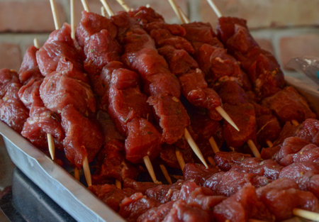 Several pieces of beef, chopped into cubes, seasoned with salt, garlic, pepper, skewered on wooden skewers, placed inside an aluminum tray.の写真素材