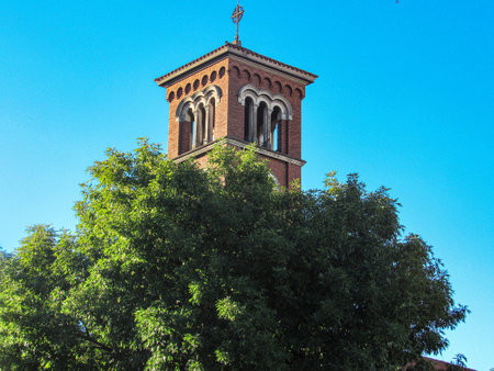 A beautiful Blue Sky, without clouds, Church behind, with its red brick tower and a stone at the top, appearing behind a tree with a robust full crown, with dark green leaves.の写真素材