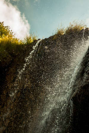 falls, the mountain river, splashes, drops on the sun, clouds in the blue skyの写真素材