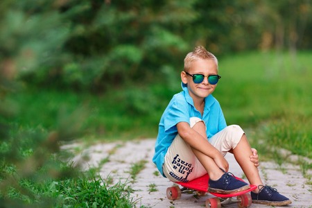 Stylish teenager boy wearing a checkered shirt and sunglasses with skateboard in city over green...