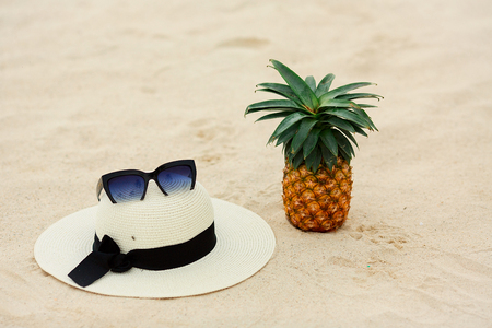 Pineapple fruit in sunglasses with hat on the sand.の写真素材