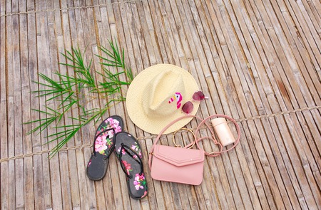 Top view: straw hat, slates, glasses, sun cream, pink female bag on bamboo branch.の写真素材