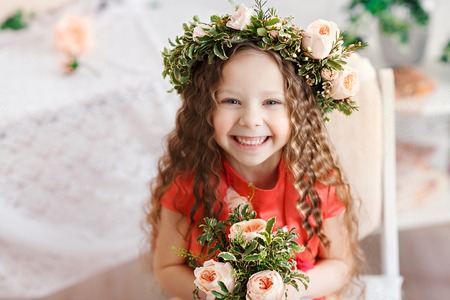 Kid in a flower crown. Cute little girl in a bright studio sits and looks into the cameraの写真素材