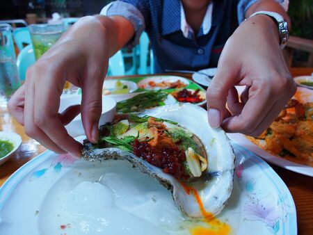 Eating raw oysters with lemon, garlic, herbs and chilli burn の写真素材
