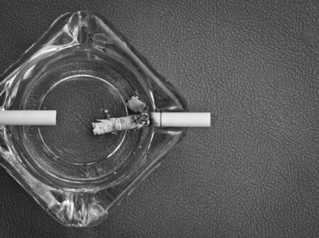 White cigarettes and clear ashtray on leather backgroundの写真素材