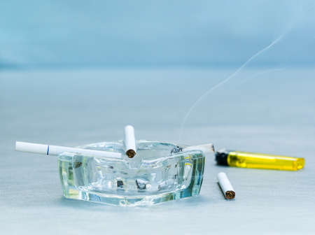 White cigarettes and clear ashtray on leather background
