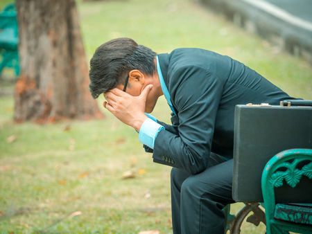 Business man sitting in outdoors park and stressed because of business work failureの写真素材