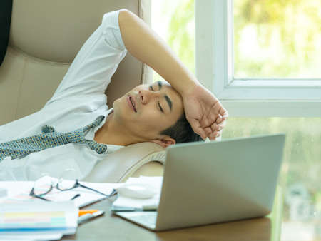 Young asian businessman tired and sleeping  after find information on the Internet, To use in business competitionの写真素材
