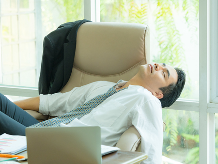Young asian businessman tired and sleeping  after find information on the Internet, To use in business competitionの写真素材