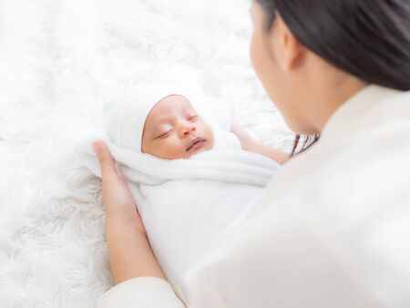 A beautiful Asian woman is looking at her newborn baby with happiness and love after a long pregnancy and just giving birthの写真素材