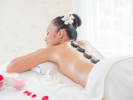 A beautiful Asian woman is relaxing in a spa shop when an expert masseuse places a hot stone on her backの写真素材