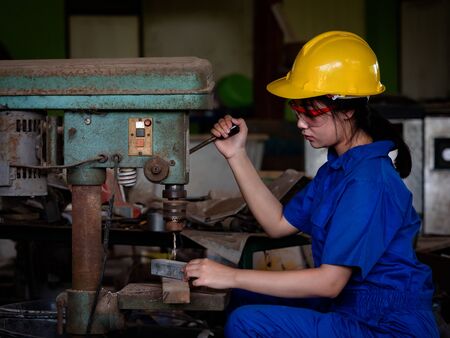 Asian women in mechanic uniforms are using power tools to drill metal bars in the factoryの写真素材