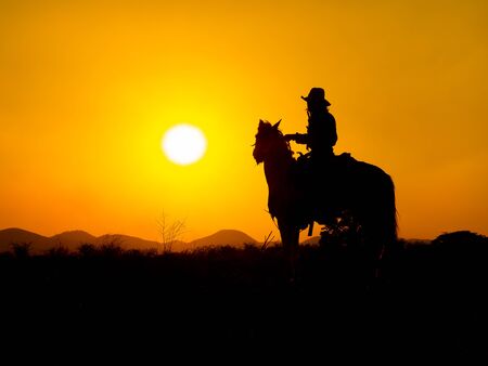 Western cowboys are sitting on horseback under the sun and preparing to use guns to protect themselves in a land that is not yet legalの写真素材