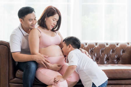 An Asian boy bent down to kiss his pregnant mother, With his father and mother looking with loveの写真素材