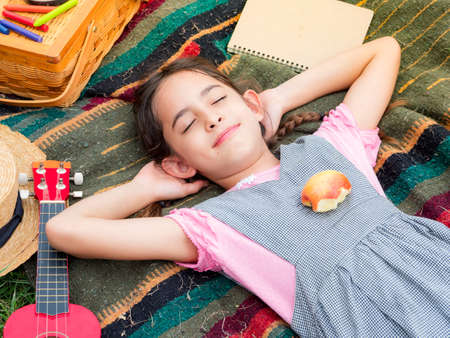 A cute girl sleeps on a blanket after playing and learning outside of school in the nature park