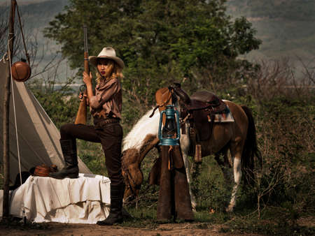A young cowgirl stand with a gun to guard the safety of the camp in the western area