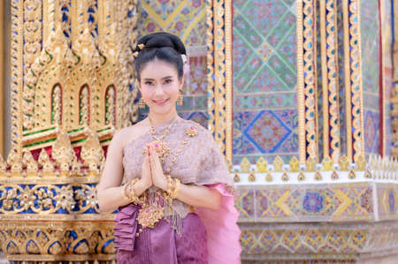 A beautiful, graceful Thai woman in Thai dress adorned with valuable jewelry raise her hand to pay respect  in a beautiful ancient Thai templeの写真素材