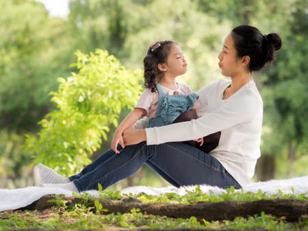 Asian little girl sitting with her mom on the cloth, Relax and learning outside of school to enjoy in the nature parkの写真素材