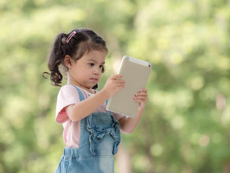 A cute Asian girl is using a tablet for fun playing games and learning outside of school in the park