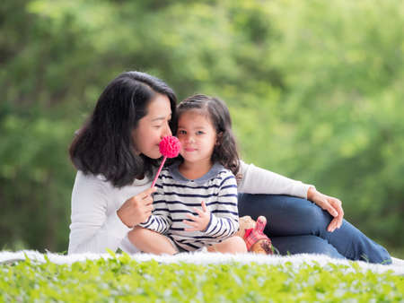 Asian little girl sitting with her mom on the cloth, Relax and learning outside of school to enjoy in the nature parkの写真素材