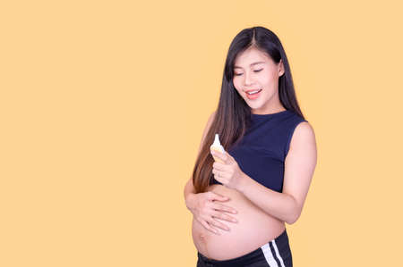 A beautiful pregnant Asian woman touches her belly and uses an ear thermometer to measure the fever...