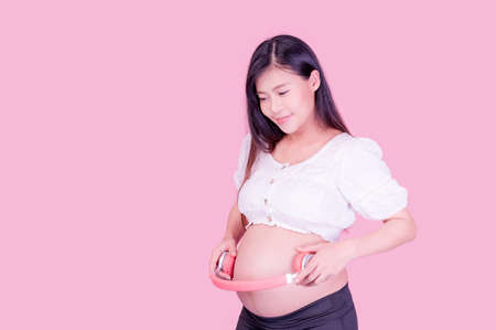 A beautiful pregnant Asian woman stands relaxed and has her unborn child listen to music with headphones connected to the Internetの写真素材