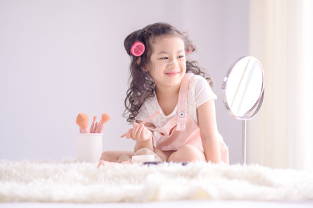 A cute little Asian girl is happily applying makeup brushes with powder in her bedroomの写真素材