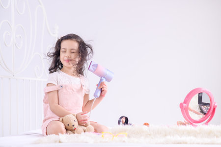 A cute Asian girl happily uses an electric dryer to blow her hair in her bedroomの写真素材