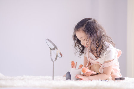 A cute little Asian girl is happily applying makeup brushes with powder in her bedroomの写真素材