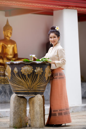 Thai woman in Thai dress stands holding lotus flower in temple During the prayer, And having fun in the water to celebrate the Songkran water festivalの写真素材