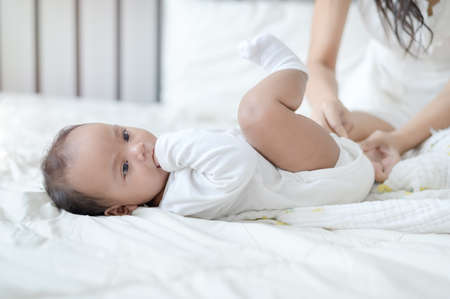 A young Asian mother is changing disposable diapers for her recently born baby daughter