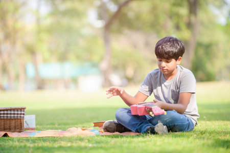 A half-Thai-Indian boy relaxes by learning to play ukulele strings while learning outside of school in a parkの写真素材